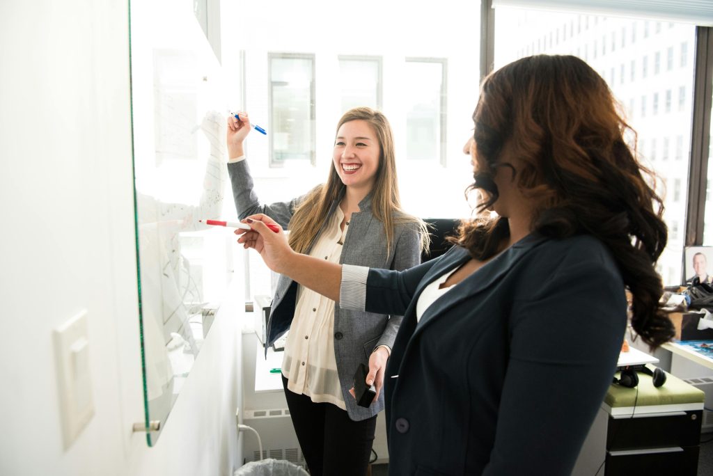 pexels photo 1181533 1181533 Two professional women discussing ideas on a whiteboard in a modern office setting.