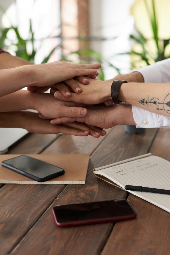 pexels photo 3184431 3184431 Hands from a diverse team stack on a table symbolizing unity and teamwork in a modern office setting.