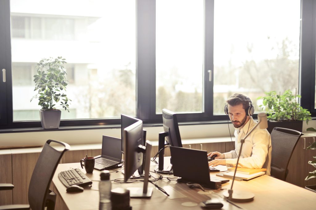 pexels photo 845451 845451 A businessman sits at a desk using multiple computers and a headset in a well-lit modern office.